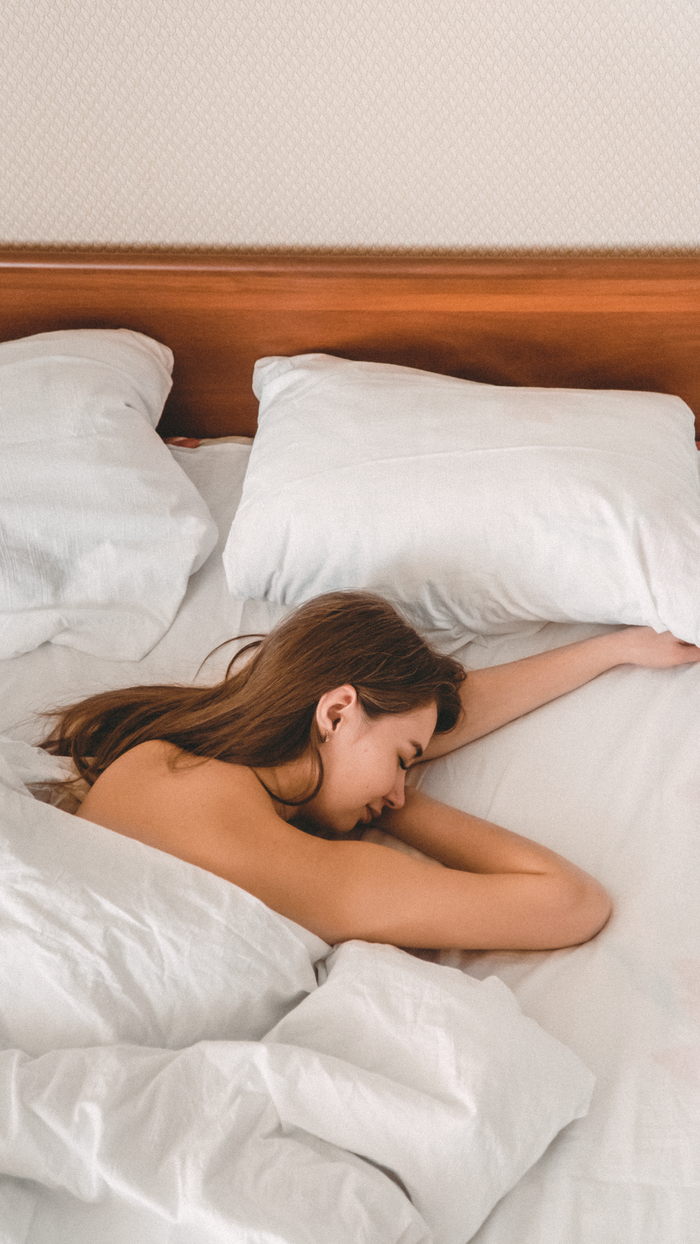 About A woman peacefully sleeping in a cozy bed with white linens, captured in a serene indoor setting.