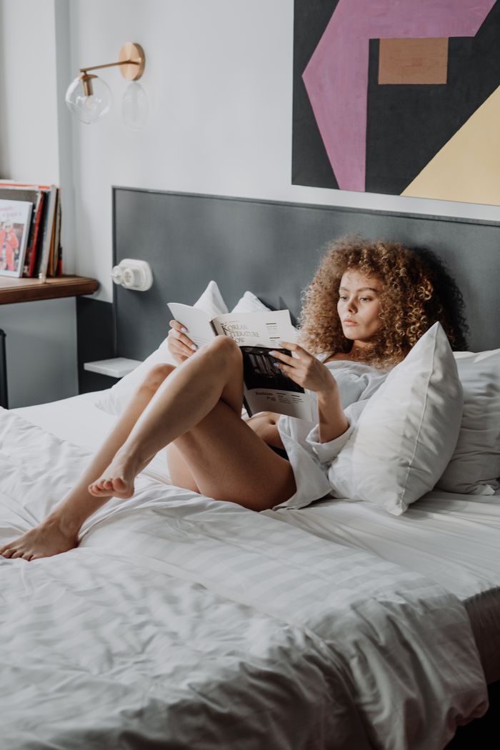 A woman with curly hair relaxes and reads on a comfortable bed in a stylish bedroom.