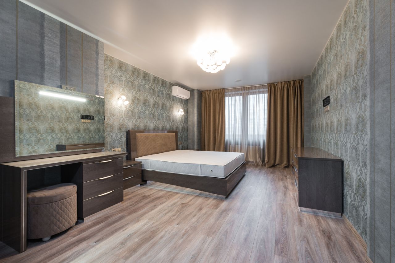 Wide angle of stylish bedroom with white mattress on bed placed near wall between cupboard with mirror and window with curtain