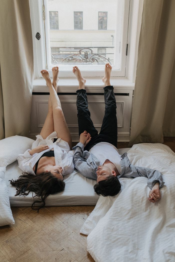 Home Romantic couple lying on a bed by the window, holding hands and enjoying a peaceful moment indoors.